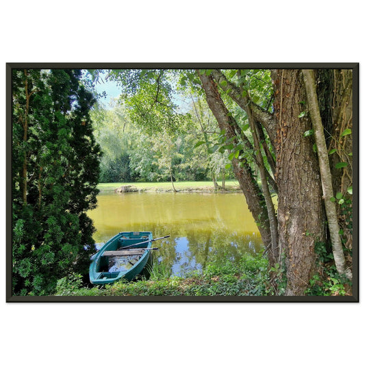 Petite barque en plastique bleu avec ses rames, amarrée au bord d'un étang paisible entouré d'arbres Photo d'art avec cadre