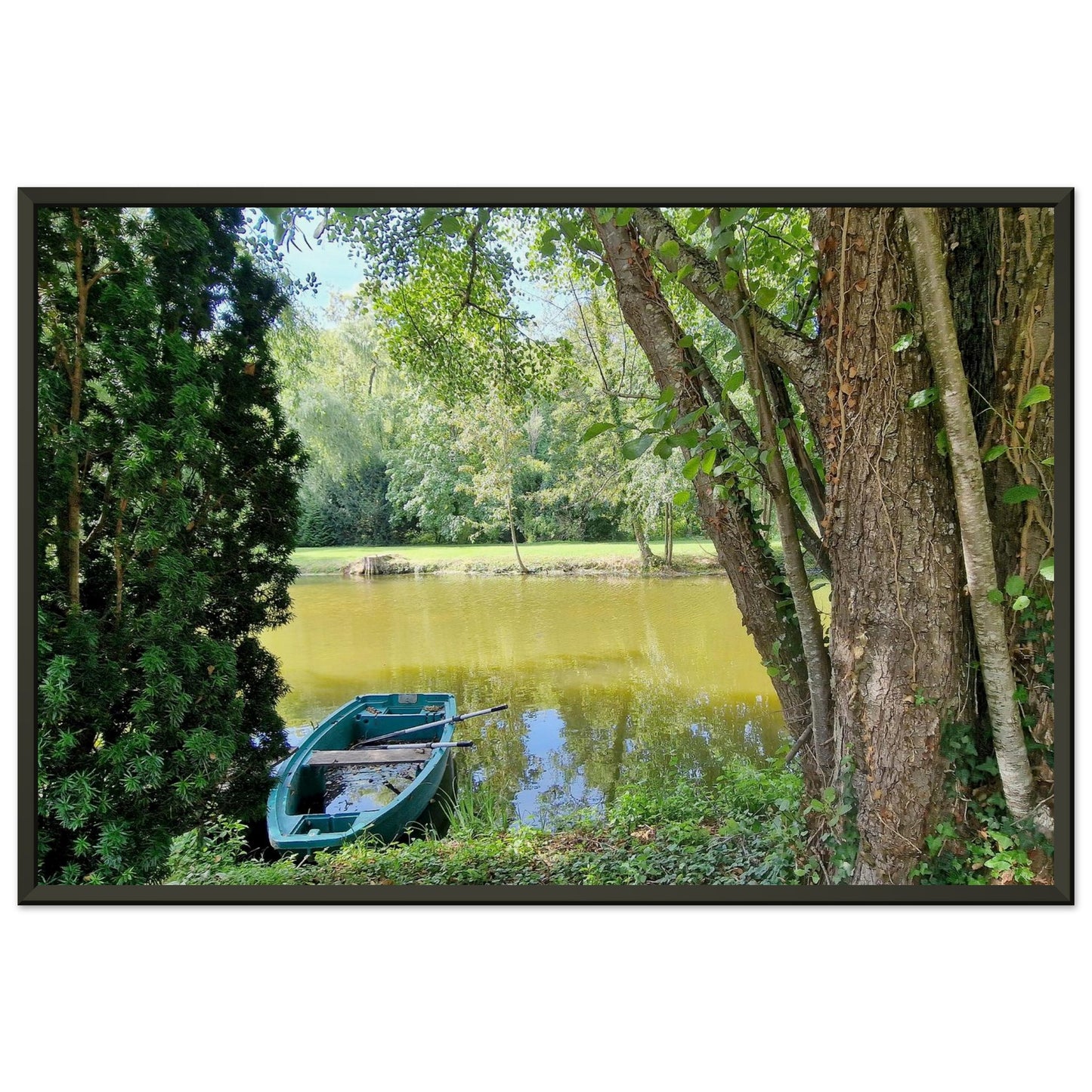Petite barque en plastique bleu avec ses rames, amarrée au bord d'un étang paisible entouré d'arbres verdoyant