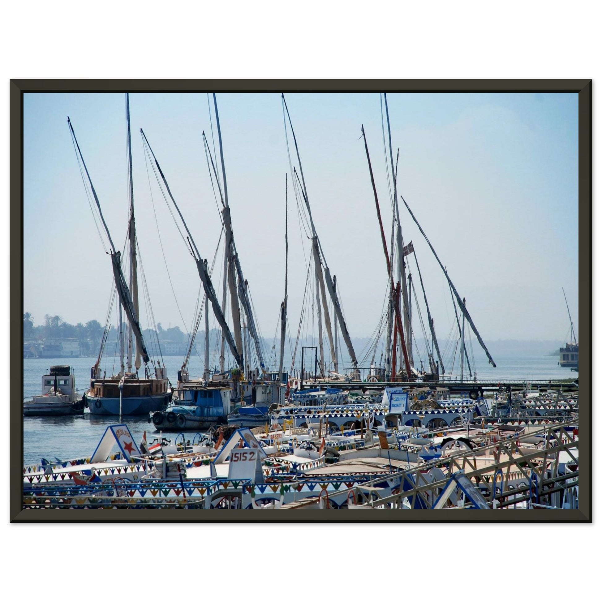 Photographie montrant un rassemblement de félouques traditionnelles égyptiennes avec leurs hauts mâtures alignés sur les rives du Nil à Louxor, sous un ciel bleu vertigineux