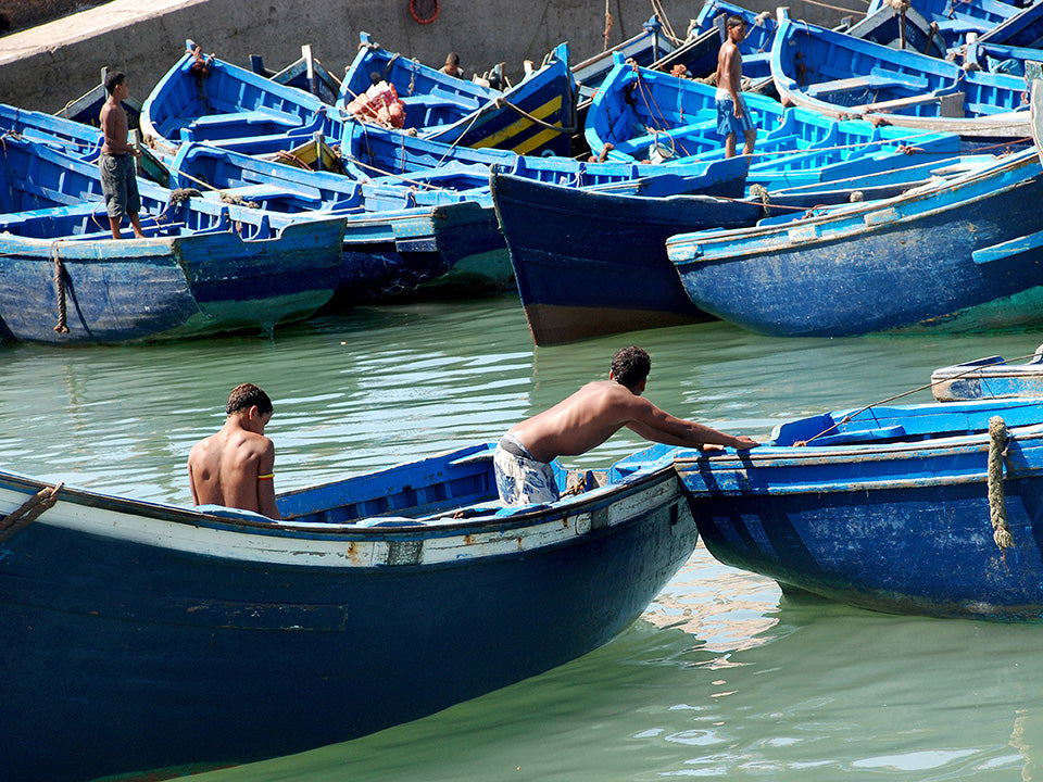 Photo d'art de jeunes garçons manoeuvrant les barques bleues de pêche traditionnelles dans le port d'Essaouira au Maroc
