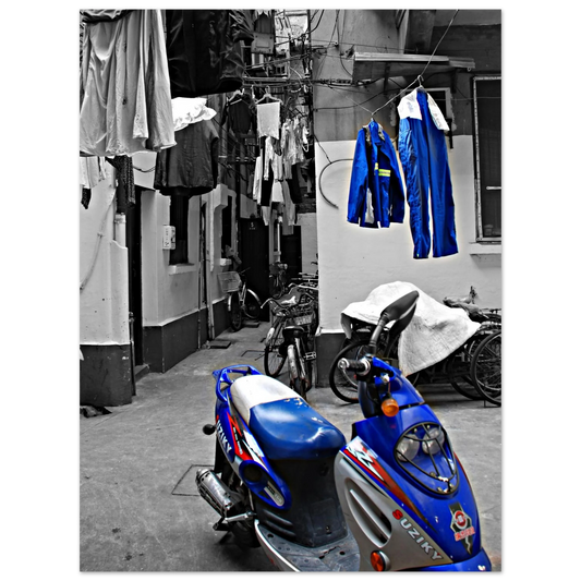 Photographie d'art en noir et blanc d'une ruelle typique de Shanghai avec un scooter bleu vif de marque Suziky et du linge suspendu en couleur sélective.